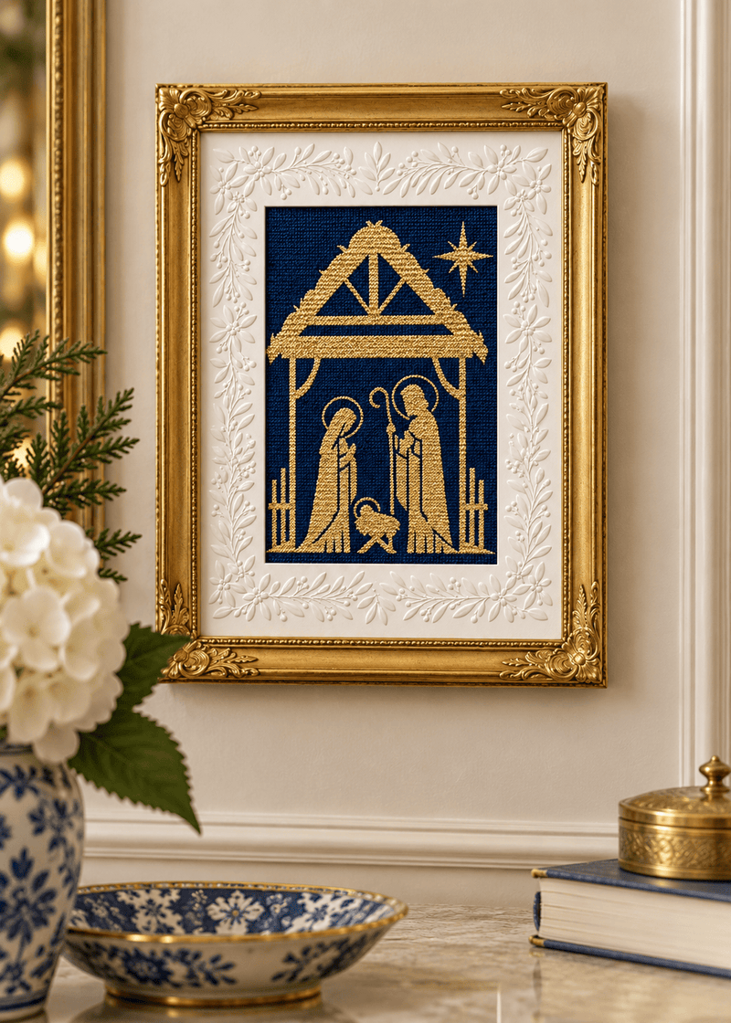 A Holy Night Nativity needlepoint in gold on navy, displayed in an ornate gold frame with a white botanical mat.